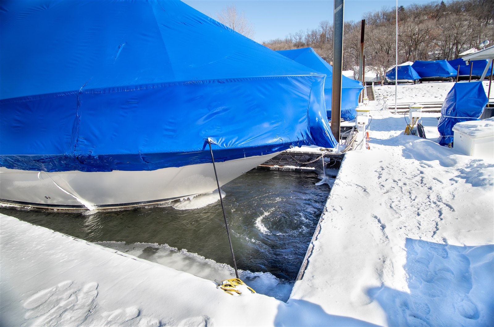 Visible water circulation beside a covered boat and snow-covered dock, with ice around the opening